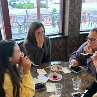 four students sitting at a table eating dessert and laughing